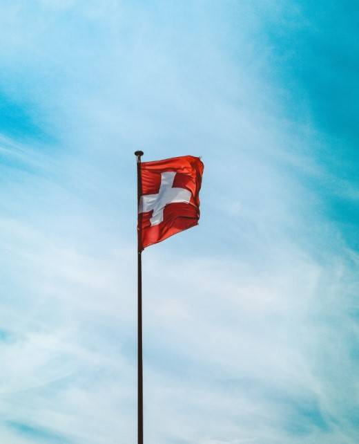 low-angle-shot-switzerland-flag-pole-breathtaking-cloudy-sky